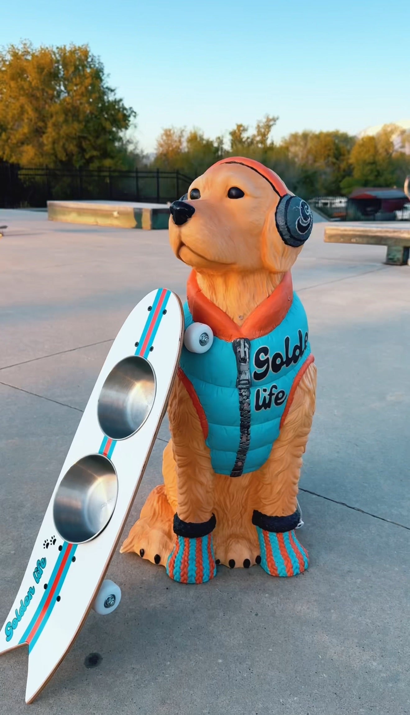 The Golden Life Kickflip Kibble Board dog feeder shaped like a skateboard with two stainless steel bowls, white board design with teal and orange racing stripes, and fixed black wheels. Get your Skateboard Dog Bowl today!