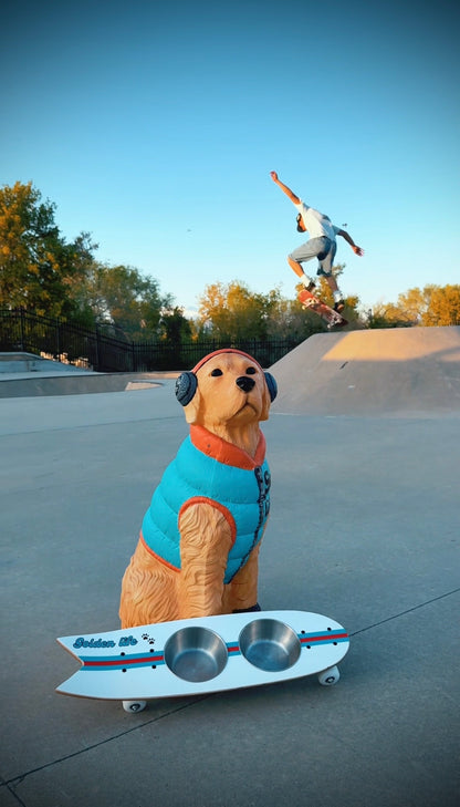 The Golden Life Kickflip Kibble Board dog feeder shaped like a skateboard with two stainless steel bowls, white board design with teal and orange racing stripes, and fixed black wheels. Get your Skateboard Dog Bowl today!