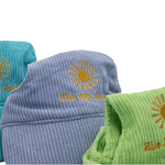 Close-up of embroidered sunburst with ‘Live Life Golden’ text on corduroy dog hats in purple, green, and teal.