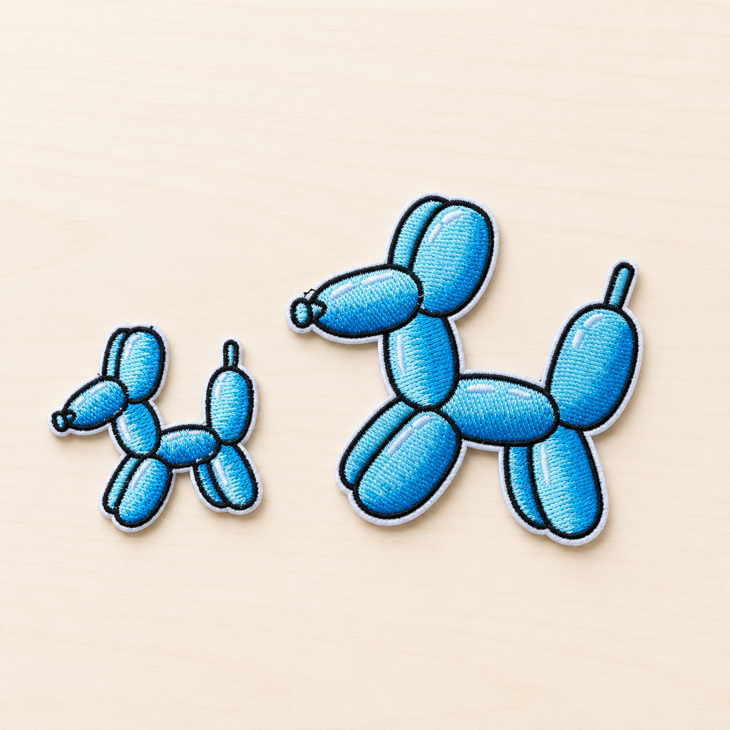 Set of two embroidered blue balloon dog iron-on patches in small and large sizes with black and white stitched borders on a light wood background.