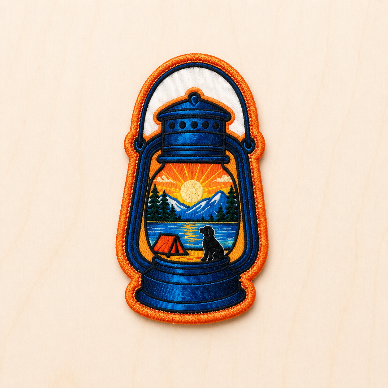 Lantern-shaped embroidered iron-on patch featuring a camping scene with mountains, lake, sunset, tent, and dog silhouette inside a blue vintage lantern with orange border on a light wood background.