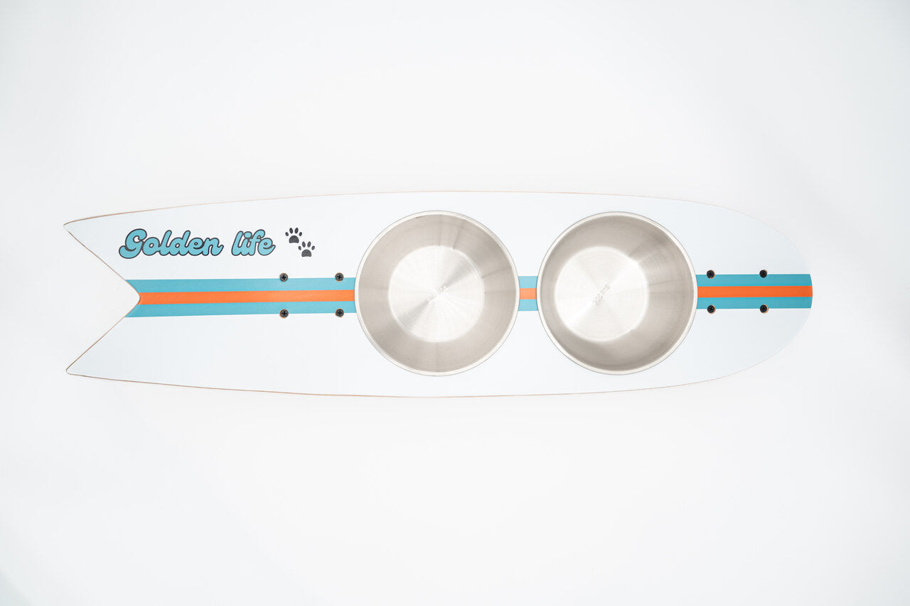 The Golden Life Kickflip Kibble Board dog feeder shaped like a skateboard with two stainless steel bowls, white board design with teal and orange racing stripes, and fixed black wheels. Get your Skateboard Dog Bowl today!