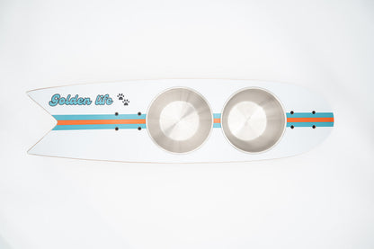 The Golden Life Kickflip Kibble Board dog feeder shaped like a skateboard with two stainless steel bowls, white board design with teal and orange racing stripes, and fixed black wheels. Get your Skateboard Dog Bowl today!