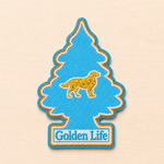 Tree-shaped embroidered patch inspired by a classic air freshener silhouette, featuring a small golden retriever icon above “Golden Life” text in light blue and white embroidery with bright blue and orange borders, displayed on a light wood surface.