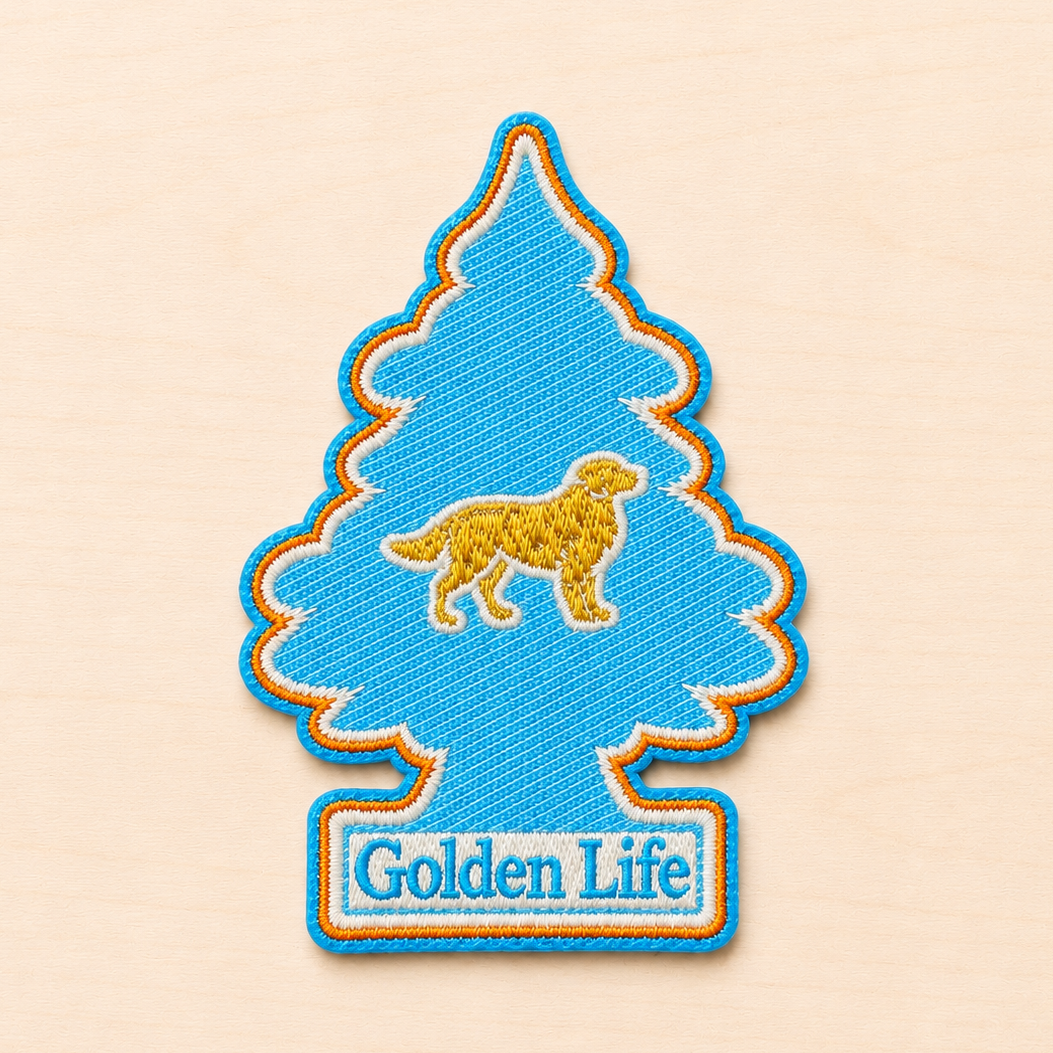 Tree-shaped embroidered patch inspired by a classic air freshener silhouette, featuring a small golden retriever icon above “Golden Life” text in light blue and white embroidery with bright blue and orange borders, displayed on a light wood surface.