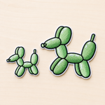 Set of two embroidered green balloon dog iron-on patches in small and large sizes with black and white stitched borders on a light wood background.