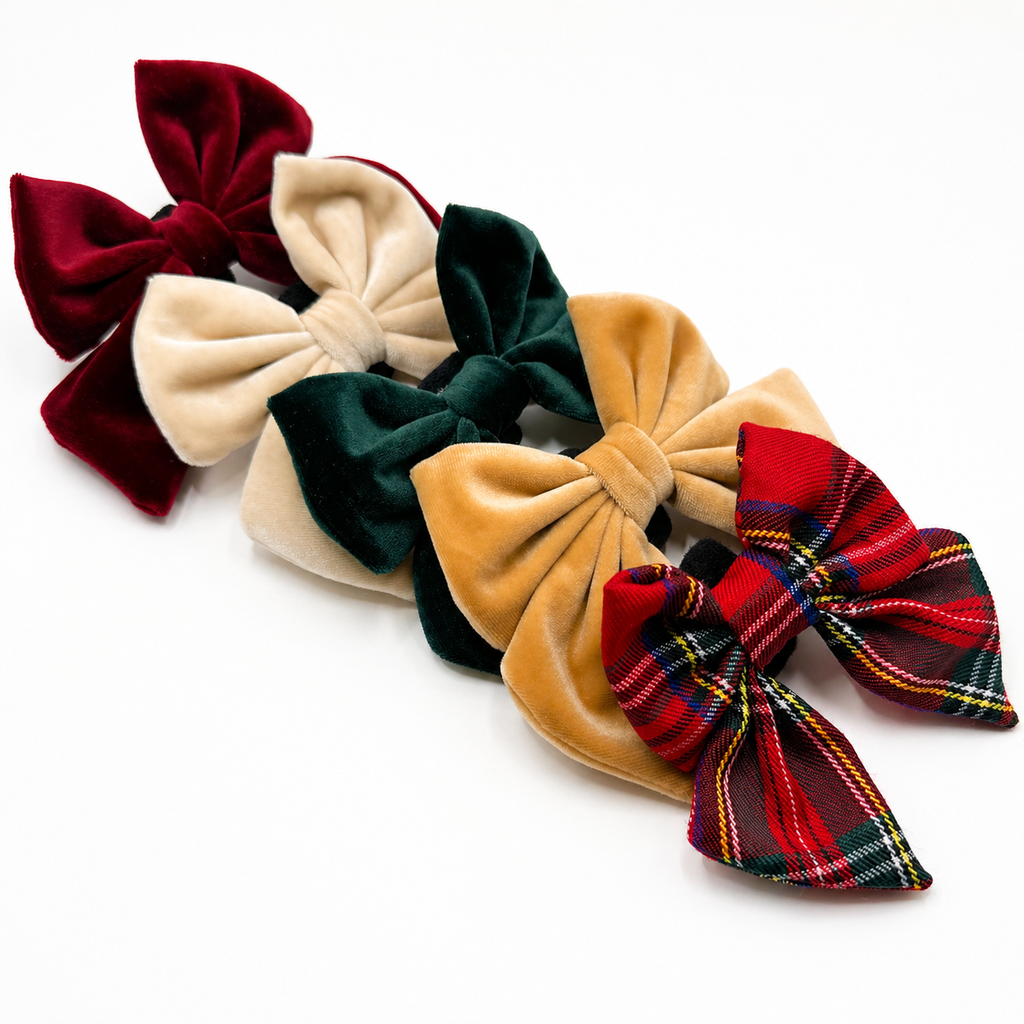 Assorted velvet dog bows in red, cream, green, gold and classic Christmas plaid arranged on a white background