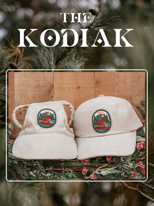 Cream corduroy human and dog hat set featuring The Kodiak adventure paddleboard iron on patch with a golden retriever, mountains, sun, and water design.