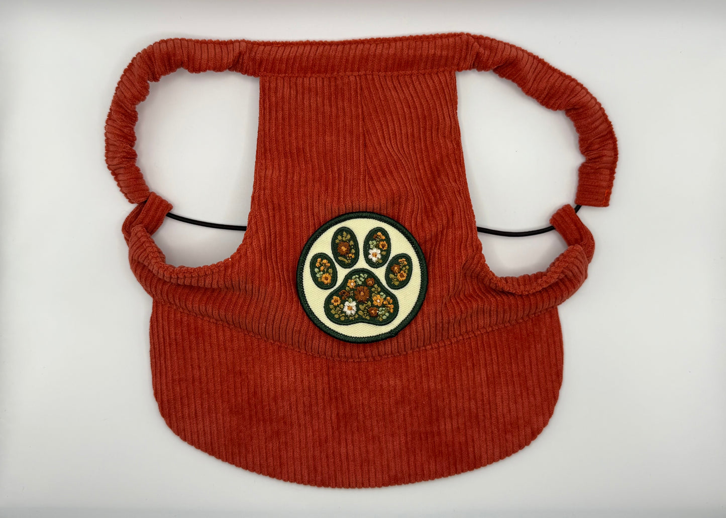 Rust-red corduroy dog hat featuring a floral paw print patch with vintage-inspired flower details — designed with adjustable straps, a curved brim, and soft corduroy texture from The Golden Life Golden Gala collection.