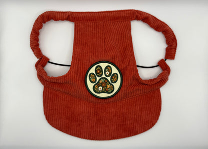 Rust-red corduroy dog hat featuring a floral paw print patch with vintage-inspired flower details — designed with adjustable straps, a curved brim, and soft corduroy texture from The Golden Life Golden Gala collection.