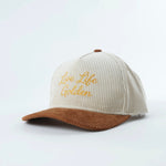 Angled view of embroidered corduroy snapback hat in cream and brown with “Live Life Golden” stitching
