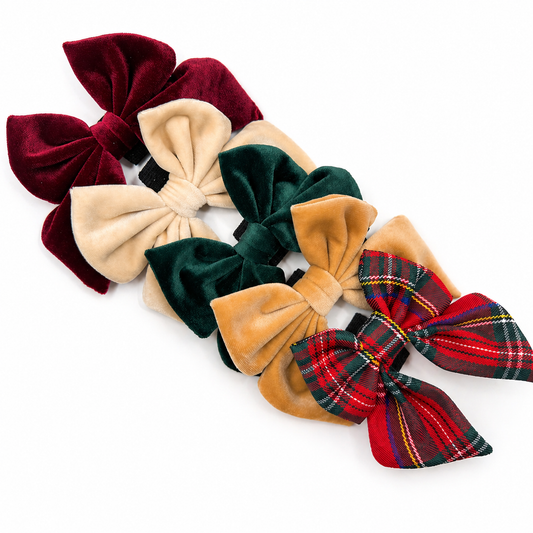 Luxury velvet dog bows in festive holiday colors including burgundy, cream, green, gold, and red plaid arranged on a white background